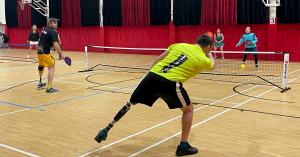 Four Ukrainian pickleball players, including three adaptive athletes with prosthetic legs, play a doubles match indoors on a hardwood court.