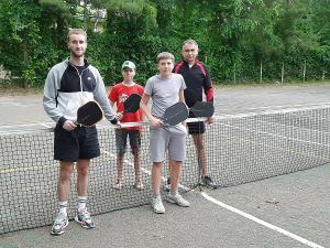 Four Ukrainian pickleball players—three teens and one adult—stand behind an outdoor net in Rivne, each holding an Anywhere Pickleball paddle.