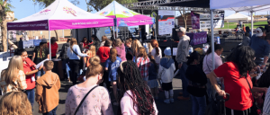 A lively outdoor event with children and families gathered around colorful tents, engaging in activities and enjoying the festive atmosphere.