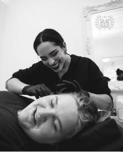 Bunny, lead piercer at Apollo Tattoo & Piercing, smiling while performing a freehand ear piercing for a relaxed client.