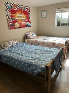 A children's bedroom with two handmade wooden Sleep in Heavenly Peace bed frames on hardwood flooring. The foreground bed has blue bedding with a polka dot pattern and matching pillow, while the background bed features colorful rainbow-patterned bedding. 