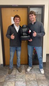 Grant Pawlak and Patrick O’Donnell smiling and giving thumbs up while holding a gray-and-black custom quilted car seat cover.