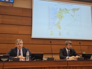 Syria expert Fabrice Balanche speaks into a microphone, explaining a map of the population concentrations in Syria, while CSI's Joel Veldkamp types to his right.
