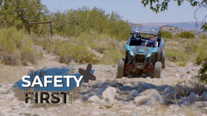 Two people in helmets and other safety gear riding in a side-by-side.