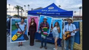 Luz Rivas team posing in colorful Lotería costumes beneath a branded canopy at a community Halloween event