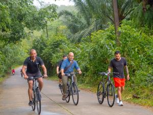 Three men, two cycling and one walking his bike, ride through a forested path during the guided bike tour to Moklen Village at Le Méridien Khao Lak Resort & Spa.