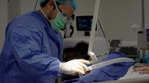 Medical professional in protective gear using a laser device on a sedated patient's burn scar during advanced scar treatment in a clinical setting.