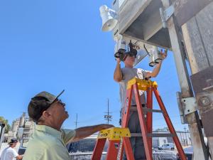 Technician installs remote video monitoring cameras at a concrete manufacturing plant in the San Fernando Valley using a pole-mounted surveillance system.