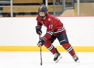 A young hockey player, with a black helmet on and a red and black hockey uniform, hitting a puck.