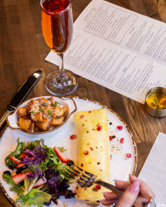 Delicious brunch near me in NYC with gourmet omelet topped with pomegranate seeds, crispy potatoes, fresh berry salad, and a sparkling cocktail at a stylish Midtown Manhattan restaurant