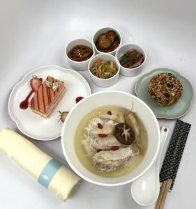 An in-flight meal featuring ginseng chicken noodle soup, a European-style bread roll with American Ginseng and Goji Berry, and an American Ginseng, Guava, and Plum Mousse dessert, accompanied by four small side dishes.