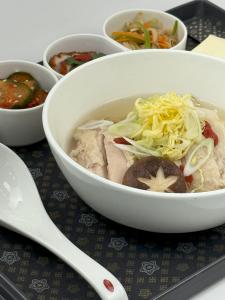 A close-up shot of ginseng chicken noodle soup with tender chicken pieces, thin noodles, goji berries, and garnished with shredded egg and chopped green onions.