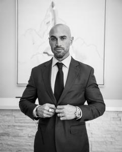 Jonathan Coyle in a tailored suit standing confidently in front of a minimalist backdrop, representing his role as a performance architect and strategic entrepreneur in regenerative health and cultural investment.