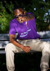 Man sitting pointing, wearing sunglasses in purple top