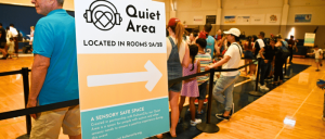 A sign for a "Quiet Area" with details about its location and purpose, in a busy event space filled with people in line.