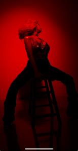 tina win models in redlights while sitting on a bar stool looking away.