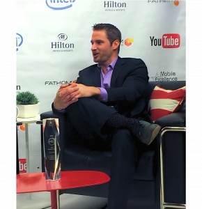 CEO of InStyler, Dan Fugardi, interviews at Youtube studios, in a suit, sitting with leg crossed over one knee, holding the other knee while talking