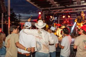Audience members gather outdoors, watching a live performance on a lit-up stage during Rock the Barn in Toronto, August 2023.