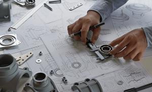 Engineer using calipers to measure a mechanical part over detailed technical drawings, surrounded by precision components and drafting tools.