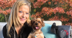 Kara smiles as she holds her rescued dog Marley, a medium-sized brown and black Yorkie pup, who sits alert and healthy. Marley, once paralyzed, has made a tremendous recovery thanks to DogSol’s red light therapy blanket. The photo captures their joyful bo