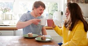 Young couple with Down syndrome smiling and enjoying tea and cake together
