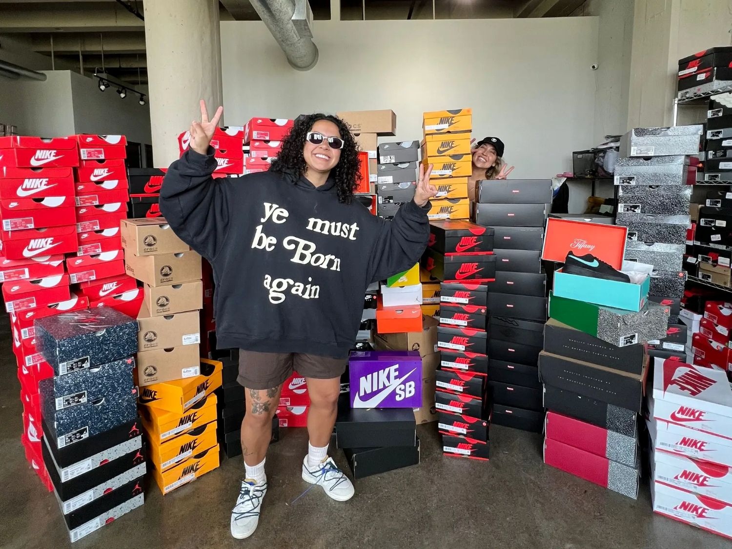 Val Zapata of The Shoe Game Co. wearing a Cactus Plant Flea Market ‘Ye Must Be Born Again’ black hoodie with Lena of GoldPawnership, showcasing luxury designer handbags from Louis Vuitton, Chanel, Goyard, Hermès, Dior, Prada, Fendi, Cartier, Rolex,Tiffany & more