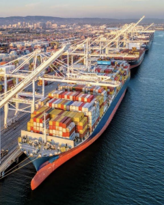 Large container ship full of cargo docked at the Port of Oakland with city in background.