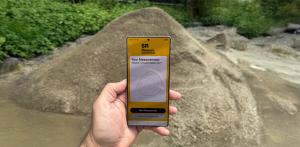 A hand holding a smartphone with a stockpile measurement on screen