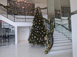 "Luxury Scottsdale interior decorated for Christmas with a grand tree and staircase wrapped in garland, featuring gold and silver ornaments and warm white lights in a modern foyer with mirrored walls and chandelier."