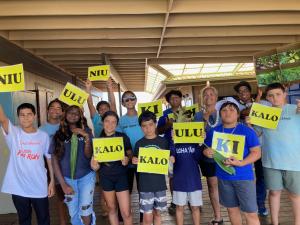 A number of youth from the island of Kaua‘i standing with mentors, with a handful of them holding yellow signs with Hawaiian words.