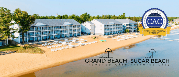 Aerial view of Grand Beach in Traverse City, featuring spacious accommodations and beach chairs along the sandy shore, plus autism certification logo.