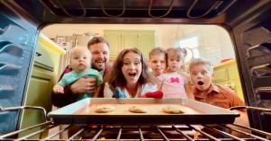 Missy Lanning pulling fresh chocolate chip cookies out of the oven while her family watches eagerly around her.