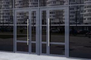 Black glass doors and windows of a modern building reflecting nearby apartment blocks across the street.