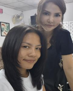 แพรวายืนอยู่ด้านหลังลูกค้าที่นั่งอยู่ในร้านของเธอในเชียงใหม่ กำลังจัดแต่งทรงผมสีเข้มที่เพิ่งตัดเสร็จอย่างตั้งใจและใส่ใจ