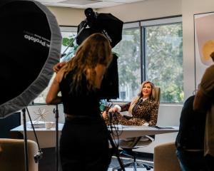 Adriana Gallardo sitting confidently at her desk during a photoshoot, surrounded by lighting equipment and crew members in an office setting.