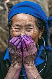 Portrait of a Hmong woman smiling with her hands stained deep purple from natural indigo dye, captured by Réhahn in northern Vietnam.