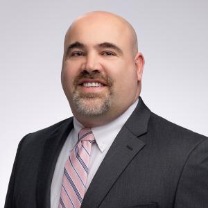 Jeremy Dobbe, attorney at Di Renzo & Bomier, smiling in a professional headshot wearing a dark suit, white shirt, and pink striped tie.