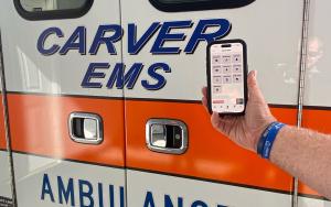Photograph of OneDose® on a mobile phone being held in front of a Carver EMS ambulance.