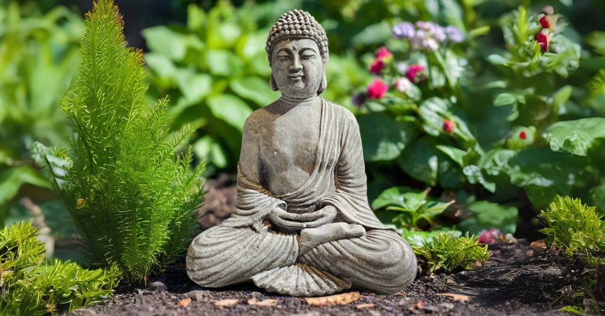 Handcrafted stone Buddha garden statue surrounded by flowers and greenery