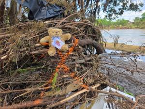 A Comfort Cub weighted, therapeutic bear sits on flood debris in Kerr County, Texas.