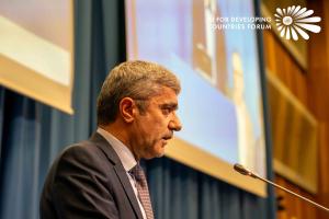 Ambassador Idibek Kalandar of Tajikistan speaking at a podium with microphone against a blue and gold backdrop with AI For Developing Countries Forum logo at the United Nations Vienna conference venue