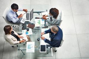 Four business people sitting around a table going over business documents and digital records.