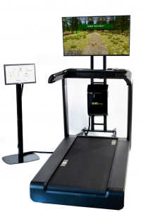 The gaitACTIVE Program is delivered through the GaitBetter system which is an add-on to existing treadmills.  The image includes a treadmill, touchscreen on a black stand, the gaitBetter black box system, and a flat screen TV on a stand.