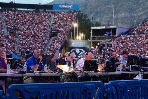 Behind-the-scenes view of Baruch Gayton producing Stadium of Fire 2025, sitting at tables with monitors and headsets, an audience of nearly 50,000 watching their production.