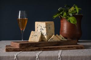 Portrait of a cut wheel of cave-aged blue cheese with a glass of ice cider.