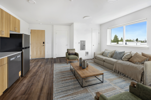 Interior view of staged one-bedroom apartment at Keystone Apartments showing modern kitchen, living area with sectional sofa, and wood-grain flooring