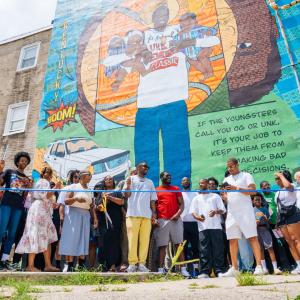 Community members gather outside Kirby Mac & Pete’s Rocks Barbershop for the unveiling of the Unk P mural designed by artist Nile Livingston in North Philadelphia