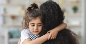 Upset little girl hugging her mom, home interior, closeup portrait.