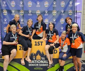 Image of a 70+ women's volleyball team on the National Senior Games podium with their gold medals.