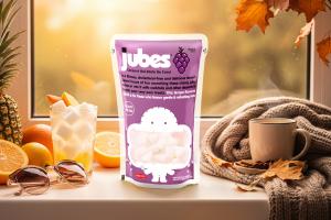A pouch of Jubes grape nata de coco placed on a windowsill surrounded by autumn leaves, sliced fruits, and a cup of tea — representing a cozy fall snack moment.